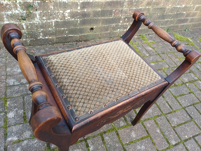 May include: An antique wooden chair with a patterned fabric seat. The chair has turned wooden armrests and legs. The dark brown wood has a rich finish, and the seat is a neutral beige colour. The chair is designed with a unique, curved shape.