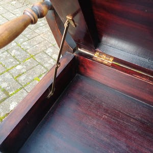 May include: An antique chest made of dark wood, featuring a hinged lid and a wooden handle. The interior is visible, showcasing the deep, rich colour of the wood. A brass support holds the lid open.