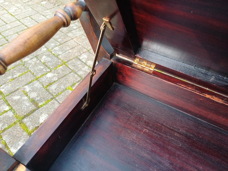 May include: An antique chest made of dark wood, featuring a hinged lid and a wooden handle. The interior is visible, showcasing the deep, rich colour of the wood. A brass support holds the lid open.
