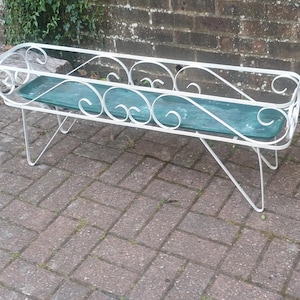 May include: White metal plant stand with a rectangular shape and decorative scrollwork. It features a teal glass insert and angled legs. A vintage-style piece for displaying plants, measuring approximately 91 cm long.