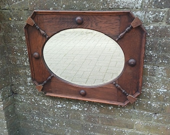 Op de afbeelding: Een antieke, achthoekige houten spiegel met een ovale spiegel. Het donkerbruine frame heeft decoratieve houten accenten, waaronder kleine knoppen en gestileerde hoekstukken. De spiegel is bevestigd aan een verweerde bakstenen muur.