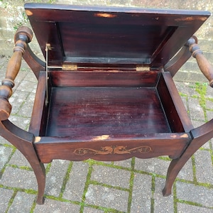May include: An antique dark brown wooden side table with a hinged lid, revealing an open storage compartment. The table has curved legs and decorative armrests. The wood shows signs of age and wear.