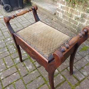 May include: A dark wooden bench with a woven seat. The bench features curved legs and armrests with turned spindles. The wood has a rich finish, and the seat has a patterned design. A classic piece of furniture.