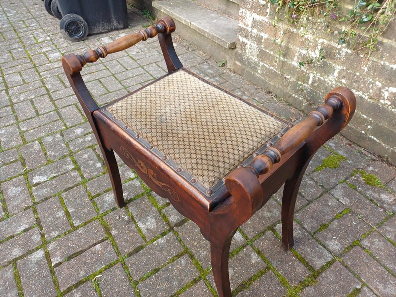 May include: A dark wooden bench with a woven seat. The bench features curved legs and armrests with turned spindles. The wood has a rich finish, and the seat has a patterned design. A classic piece of furniture.