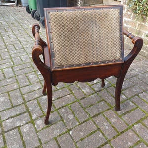 May include: An antique wooden chair with a patterned fabric back and seat. The chair has curved armrests and legs, and is made of dark wood. The back of the chair is rectangular and the seat is square.