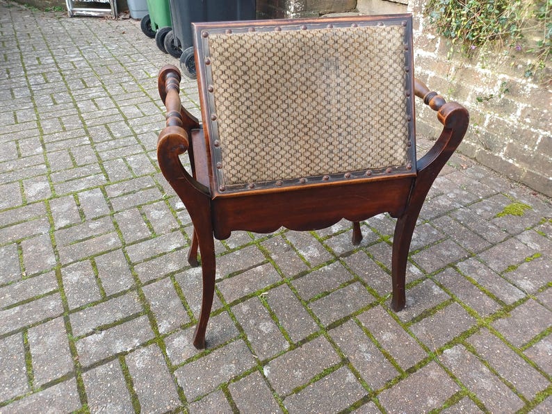 May include: An antique wooden chair with a patterned fabric back and seat. The chair has curved armrests and legs, and is made of dark wood. The back of the chair is rectangular and the seat is square.