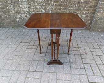 May include: A dark brown, antique drop-leaf table with a rectangular top and four slender legs. The table has a central support structure and is made of wood. The table is approximately 30 inches long when fully extended.