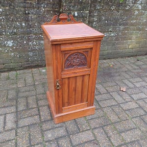 May include: A vintage wooden cabinet with a carved floral design on the door. The cabinet has a single door and a top shelf. The cabinet is made of dark wood and has a distressed finish.