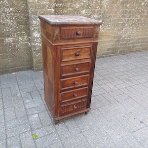 May include: An antique wooden cabinet with six drawers and a marble top. The cabinet is a rich brown colour, with carved details on the top drawer and a decorative pattern on the marble. It stands on a grey tiled surface.