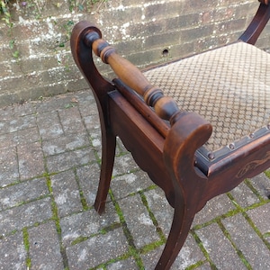 May include: An antique wooden chair with a patterned seat and curved armrests. The chair features dark brown wood with decorative carvings and a light-coloured patterned fabric. The legs are curved, and the chair appears well-preserved.