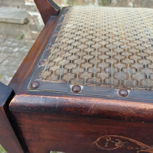 May include: Close-up of a vintage wooden chair with a patterned seat. The dark brown wood frame features decorative carvings and metal studs along the seat's edge. The seat has a beige and brown geometric pattern.