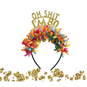 May include: A gold glitter headband with the text "Oh Shit I'm 80" on top. The headband is decorated with colorful tissue paper streamers.