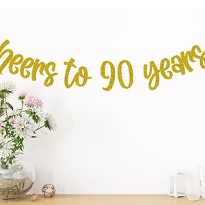May include: Gold glitter banner with the text "Cheers to 90 years".