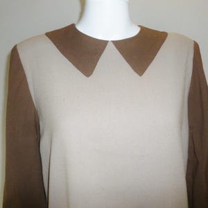 May include: A two-tone dress with a light beige body and brown sleeves. The dress features a contrasting brown Peter Pan collar. The long sleeves and collar are a darker shade of brown than the body of the dress.