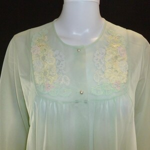 May include: A light green vintage nightgown with floral embroidery in yellow, white, and pink. The nightgown has a round neckline and long sleeves. It is buttoned down the front with three small buttons.