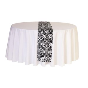 May include: A white round tablecloth with a black and white damask patterned table runner.