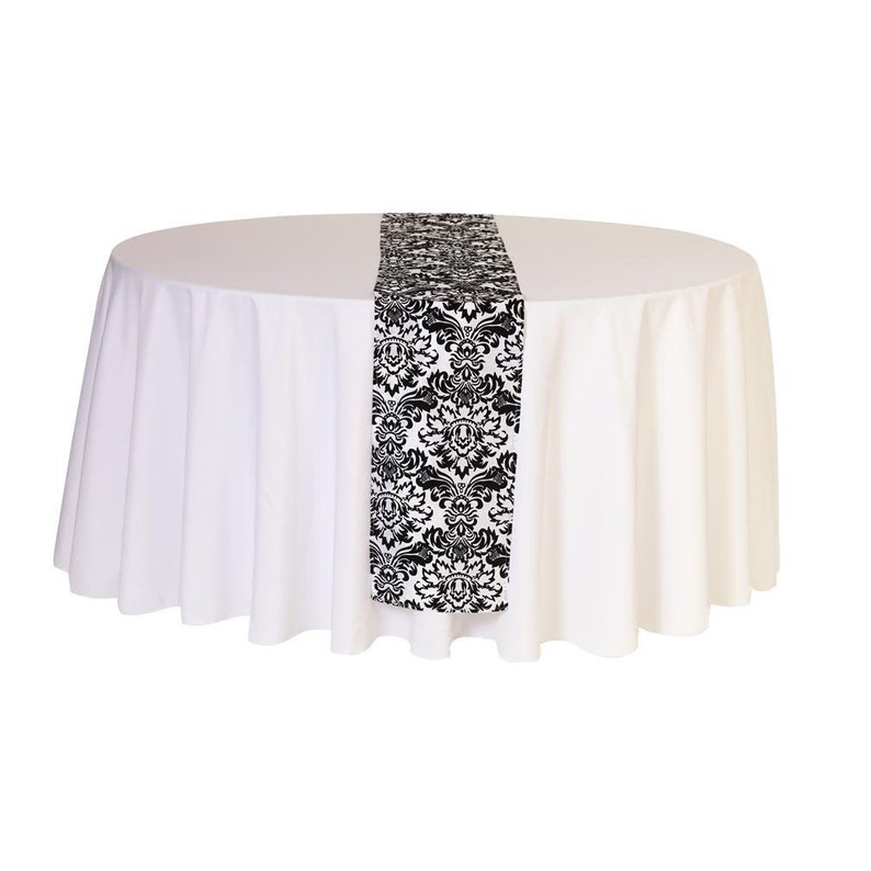 May include: A white round tablecloth with a black and white damask patterned table runner.