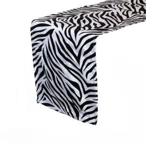 May include: A black and white zebra print table runner. The runner is made of a satin-like fabric and has a subtle sheen.