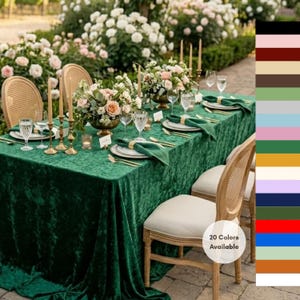 May include: A dark green velvet tablecloth draped over a rectangular table set for a formal event. The table features white chairs with cane backs, floral centerpieces, gold taper candle holders, white plates, and green velvet napkins.