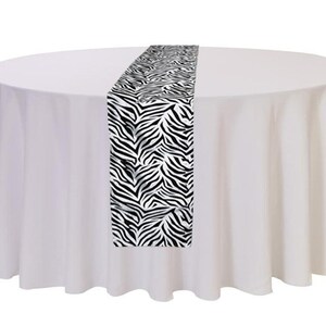May include: A white tablecloth with a black and white zebra print table runner. The table runner is 14 inches wide and 72 inches long.