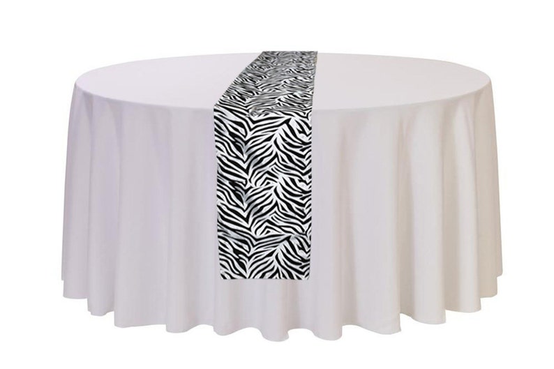 May include: A white tablecloth with a black and white zebra print table runner. The table runner is 14 inches wide and 72 inches long.