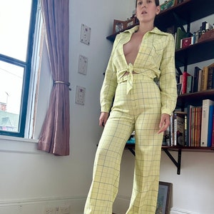 May include: A yellow and blue plaid pantsuit with a long-sleeved shirt and wide-leg pants. The shirt has a tie at the waist.
