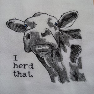 May include: A white kitchen towel with a black and white embroidered image of a cow's head with the text "I herd that."