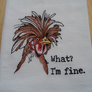 May include: Embroidered kitchen towel featuring a brown and white chicken with a large, fluffy crest. The chicken is looking to the right and the text "What? I'm fine." is embroidered below the chicken.