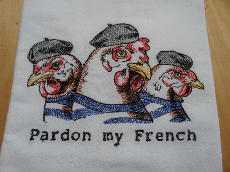 May include: Three embroidered chickens wearing blue and white striped berets and scarves with the text "Pardon my French" below them.