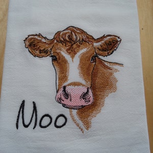 May include: Embroidered kitchen towel featuring a brown and white cow with a pink nose. The towel has the word "Moo" embroidered below the cow.