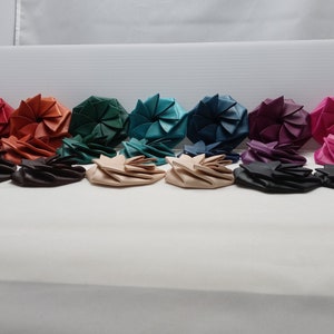 May include: A collection of 10 colorful fabric coin purses in various shades of red, orange, green, blue, purple, and pink. The purses are folded into a flower shape and arranged in a row.