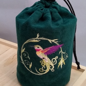 May include: A green velvet drawstring bag with a black drawstring and a gold embroidered hummingbird on a branch.