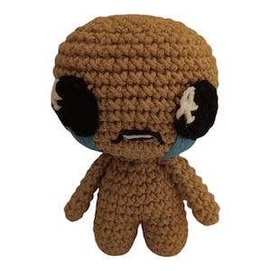 May include: A crocheted brown toy with a sad expression. The toy has black eyes with white accents and blue tear-shaped details.