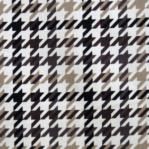 May include: Close-up of a fabric with a classic houndstooth pattern. The design features a repeating pattern of black, brown, and tan shapes on a white background. The fabric has a woven texture.