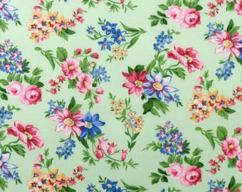 May include: A light green fabric with a repeating floral pattern. The design features clusters of pink, red, blue, and yellow flowers with green leaves. The flowers are of various sizes and shapes, creating a dense, all-over pattern.