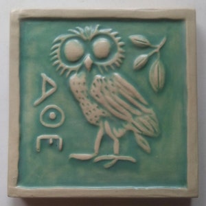May include: Square ceramic tile with a teal background and a raised relief design of an owl, a sprig of leaves, and Greek letters. The owl is off-white, and the tile has a cream-colored border.
