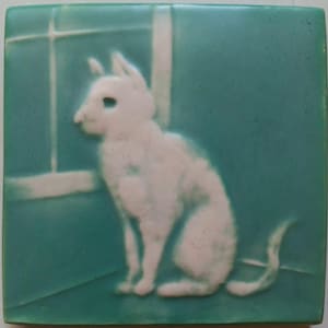 May include: A square ceramic tile featuring a raised white relief of a cat sitting in profile. The cat is positioned in front of a window frame design. The background of the tile is a solid teal color, providing a contrast to the white cat figure.