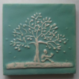 May include: Square ceramic tile with a teal background and a raised white design. The design features a tree with a person reading beneath it. The tile has a textured surface and a light-colored border.