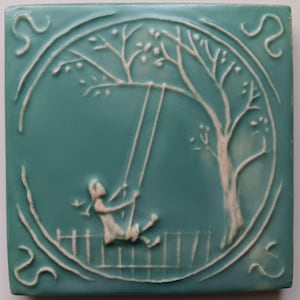 May include: Square ceramic tile with a teal background and a raised white design. The design features a child on a swing under a tree, enclosed in a circular frame. Decorative swirls are in each corner.