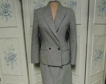 May include: A gray double-breasted blazer and matching skirt suit. The blazer has two buttons and a black trim around the collar and pockets. The skirt is knee-length.