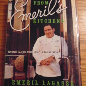 May include: A cookbook titled "From Emeril's Kitchen" featuring a photo of Emeril Lagasse in a chef's coat. The cover is black with white and green text. The book promises favorite recipes from Emeril's Restaurants.