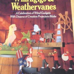 May include: A book cover titled "Whirligigs & Weathervanes" with a brown background and colorful wooden cutouts of wind-powered gadgets. The cover features a windmill, train, and marching band figures. The authors are David Schoonmaker & Bruce Woods.
