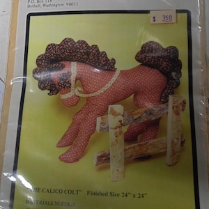 May include: Calico Colt sewing pattern by Nancy Southerland-Holmes. The pattern is for a 24 inch by 24 inch calico colt. The pattern includes instructions for making the body, mane, tail, eyelashes, ears, bridle, and legs. The pattern also includes instructions for making a fence for the colt to stand behind. The pattern costs $3.50.