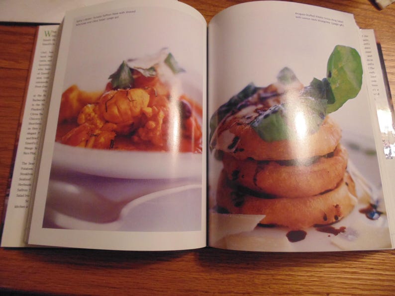 May include: Two-page spread from a cookbook featuring two food dishes. The left page shows a white bowl with a reddish-orange dish. The right page displays a stack of golden-brown food items with a dark sauce and green garnish.