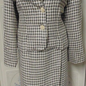 May include: A white and brown houndstooth patterned blazer and skirt set. The blazer has a notched collar and a button closure. The skirt is a-line and hits above the knee.