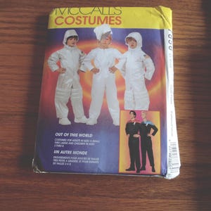 May include: A vintage McCall's Costumes sewing pattern. The package features illustrations of three children in white space suits and two adults in Star Trek-style uniforms. Text includes "Out of this World" and "Un Autre Monde".