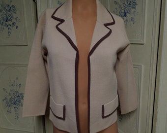 May include: A cream-colored knitted cardigan with brown trim around the collar, pockets, and edges. The cardigan is open in the front and has a relaxed fit.