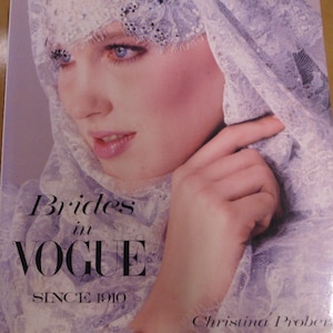 May include: A book cover showing a woman with blue eyes and a pale complexion, wearing a white lace veil. The title "Brides in VOGUE SINCE 1910" is in black text. The author's name, Christina Prober, is also visible.