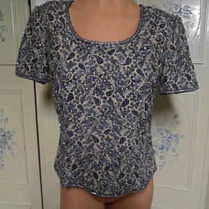 May include: A short-sleeved, sequined top with a scoop neck and a paisley pattern in shades of black and silver.