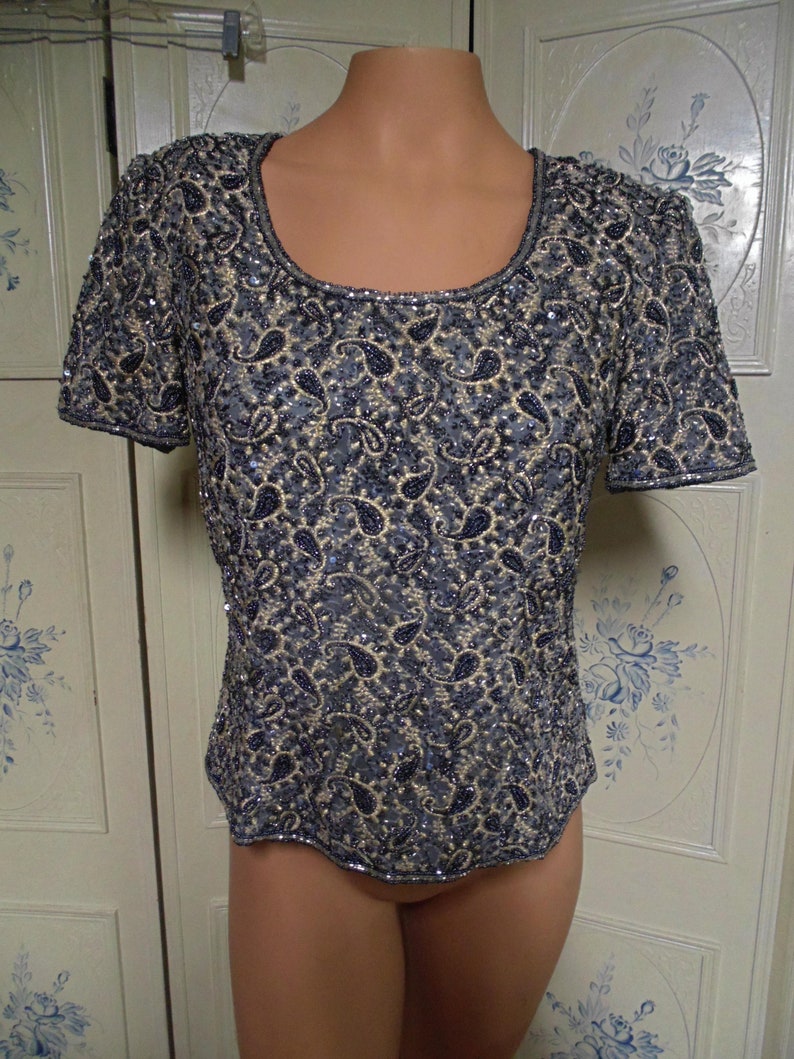 May include: A short-sleeved, sequined top with a scoop neck and a paisley pattern in shades of black and silver.